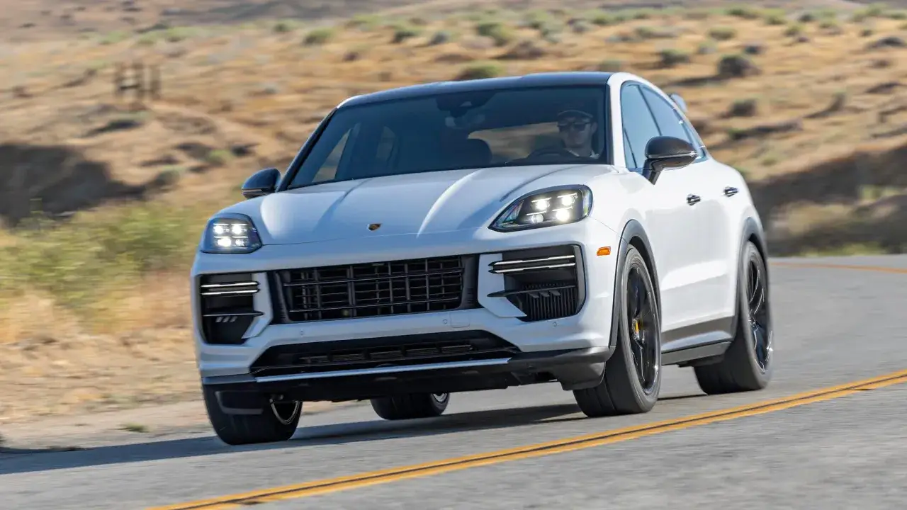 Biały Porsche Cayenne Turbo GT z czarnym dachem pędzi po krętej drodze wśród pustynnych wzgórz.