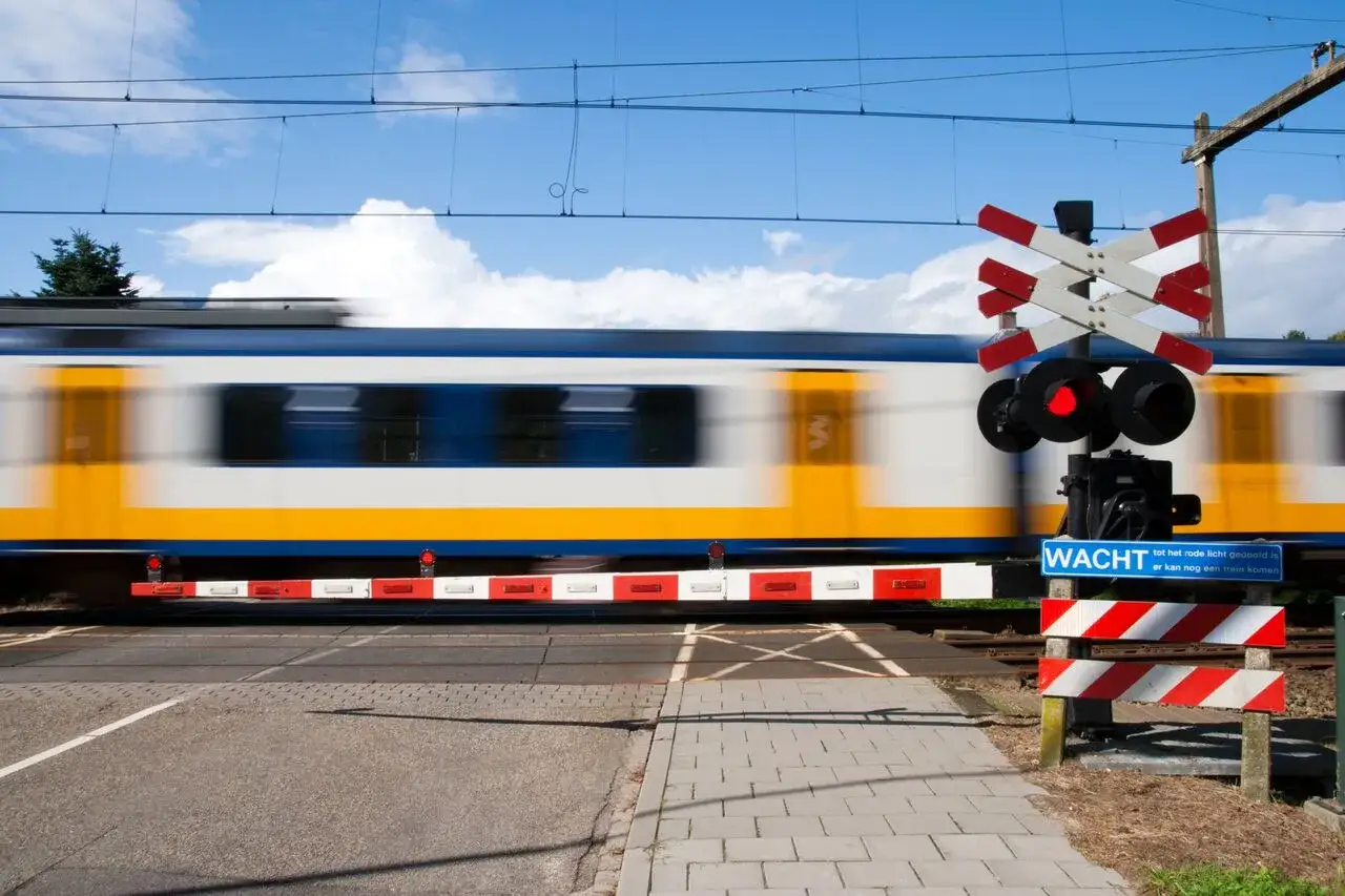 Pędzący pociąg mija przejazd kolejowy z zaporami. Czerwone światło sygnalizuje, że zbliża się kolejny skład.
