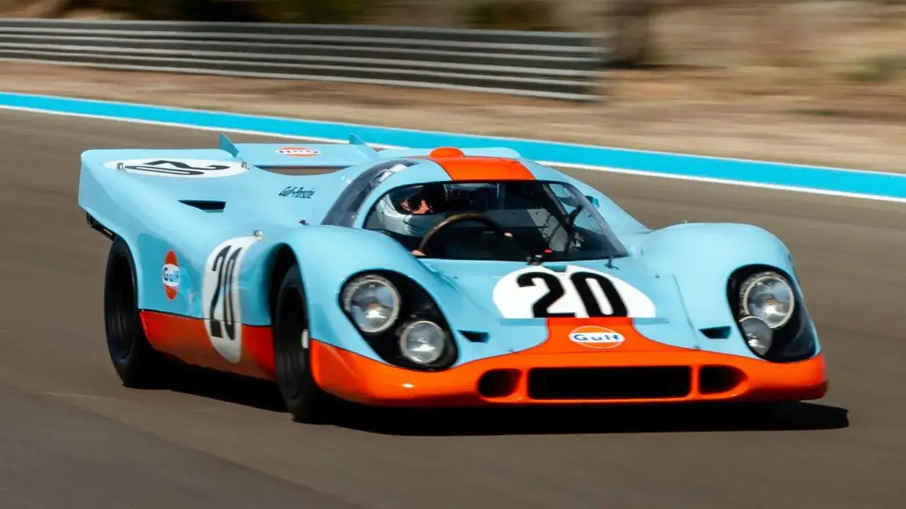 Legendarny Porsche 917 w barwach Gulf pędzi po torze, z kierowcą w kasku za sterami.