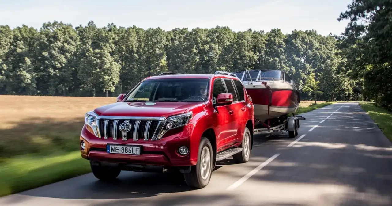 Czerwony SUV z przyczepą i łodzią na drodze. Kierowca z kodem 96 prawo jazdy wiezie sprzęt wodny na wakacje.