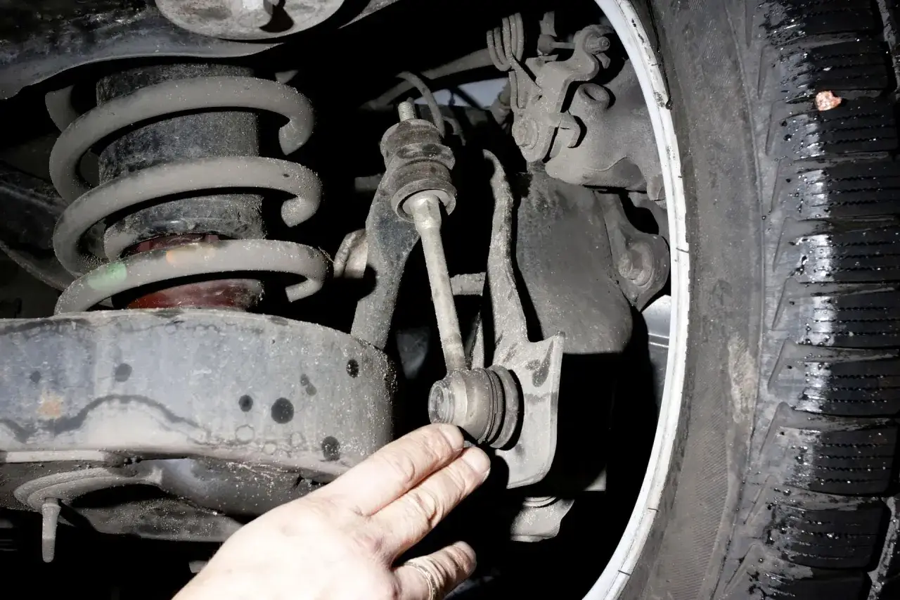 Dłoń mechanika wskazuje na łącznik stabilizatora w zawieszeniu samochodu.