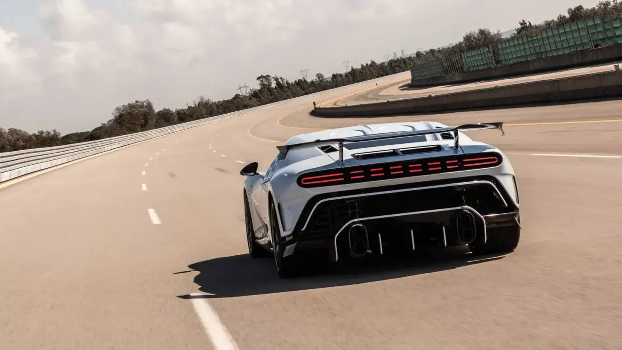 Biały Bugatti Centodieci z charakterystycznym tylnym spojlerem i światłami LED pędzi po zakręcie toru wyścigowego.