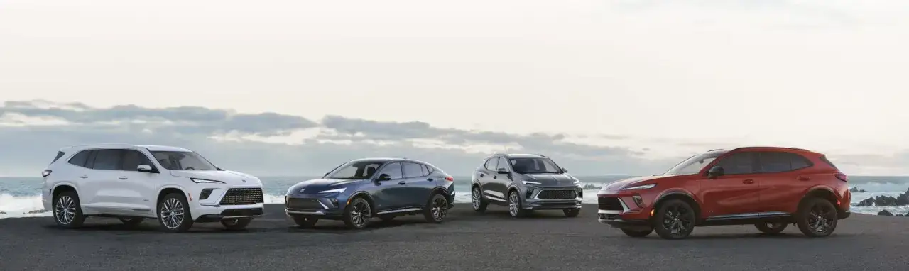 Cztery nowe modele Buick stoją przy oceanie. Biały, granatowy, szary i czerwony Buick prezentują nowoczesny design.