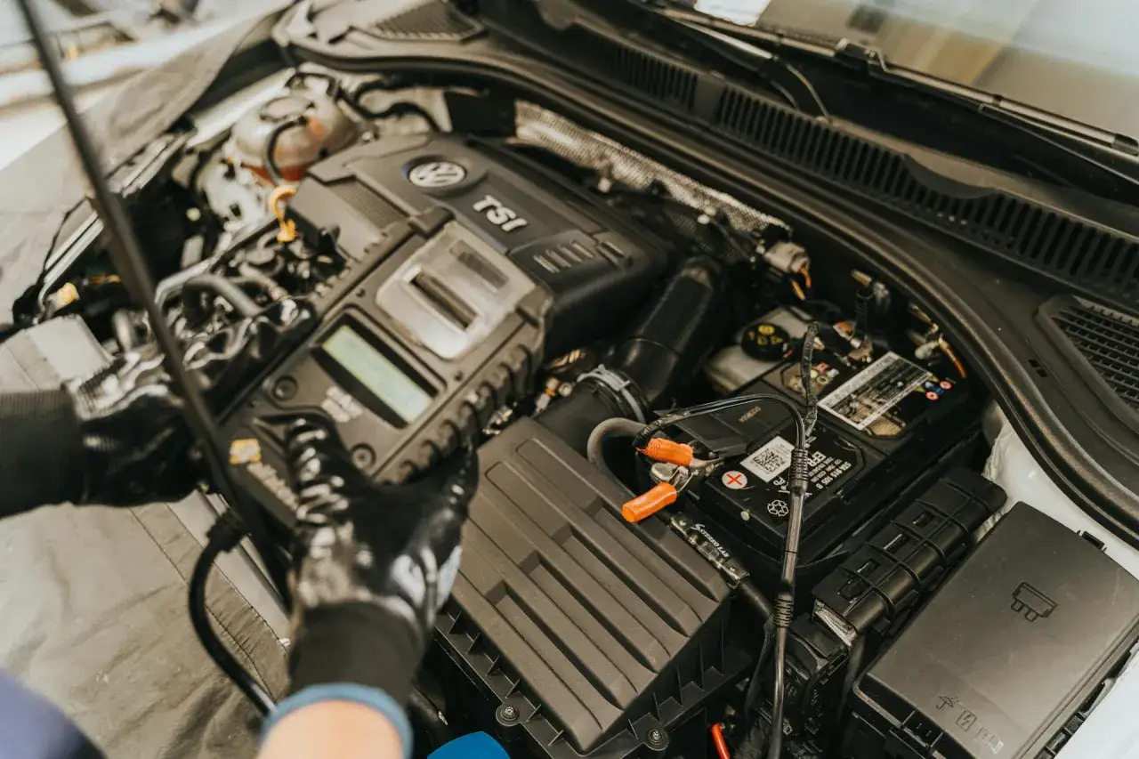 Mechanik w rękawiczkach podłącza tester do akumulatora samochodu, sprawdzając jego rezystancję.