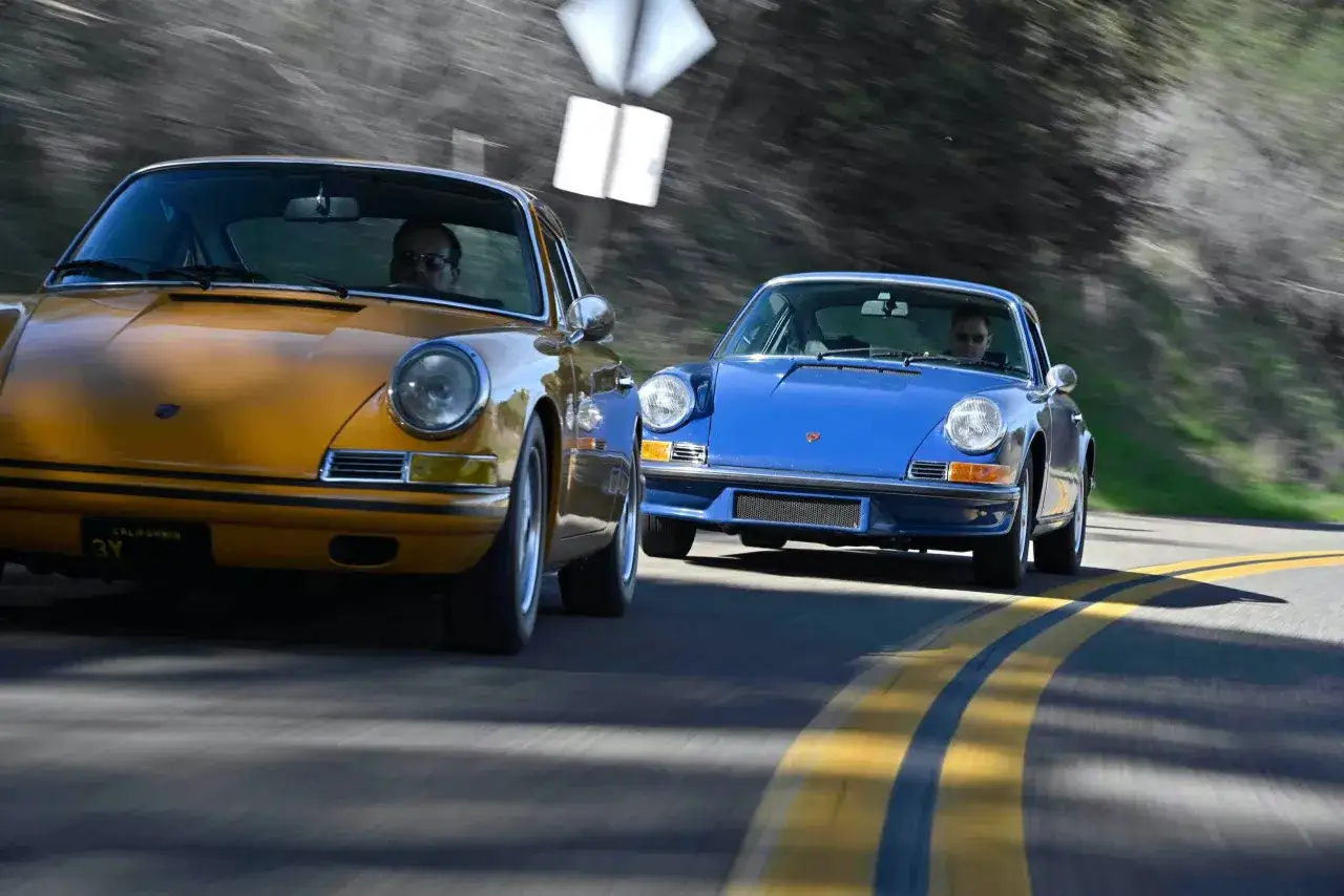 Dwa klasyczne Porsche 912, żółte i niebieskie, pędzą po krętej drodze.