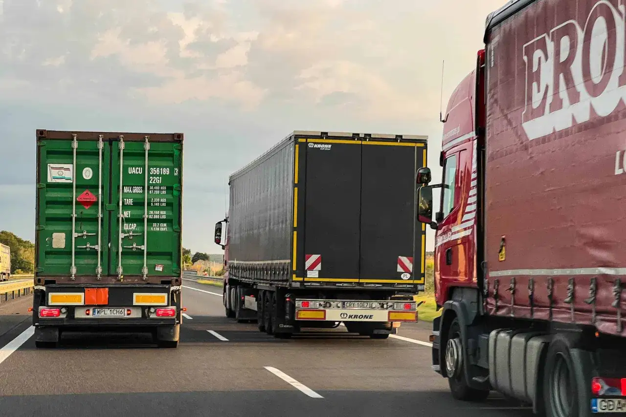 Trzy ciężarówki jadące autostradą. Znak zakazu wyprzedzania dla ciężarówek jest widoczny na drodze.