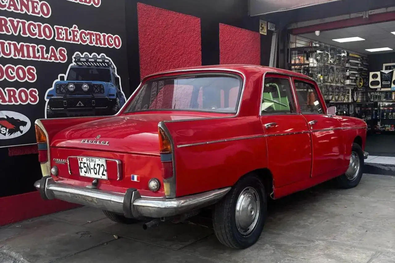 Klasyczny czerwony Peugeot 404 z Peru, z zielonym wnętrzem, zaparkowany przed sklepem z częściami samochodowymi.