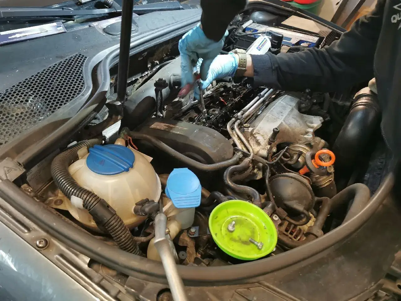 Mechanik w niebieskich rękawiczkach dokonuje wymiany świec zapłonowych w silniku samochodu.