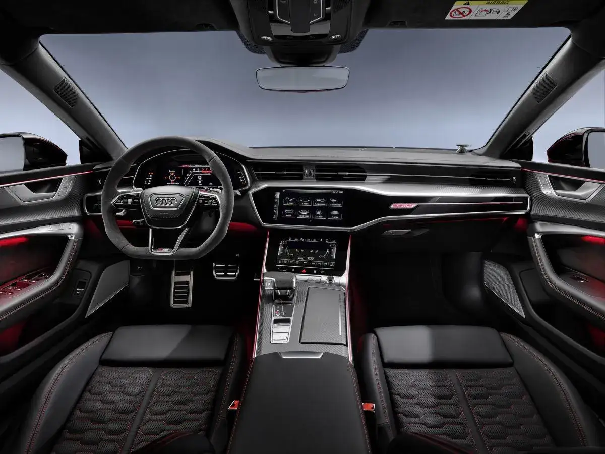 Wnętrze Audi RS7 Sportback: czarne fotele z czerwonym przeszyciem, sportowa kierownica, cyfrowe zegary i ambientowe oświetlenie.
