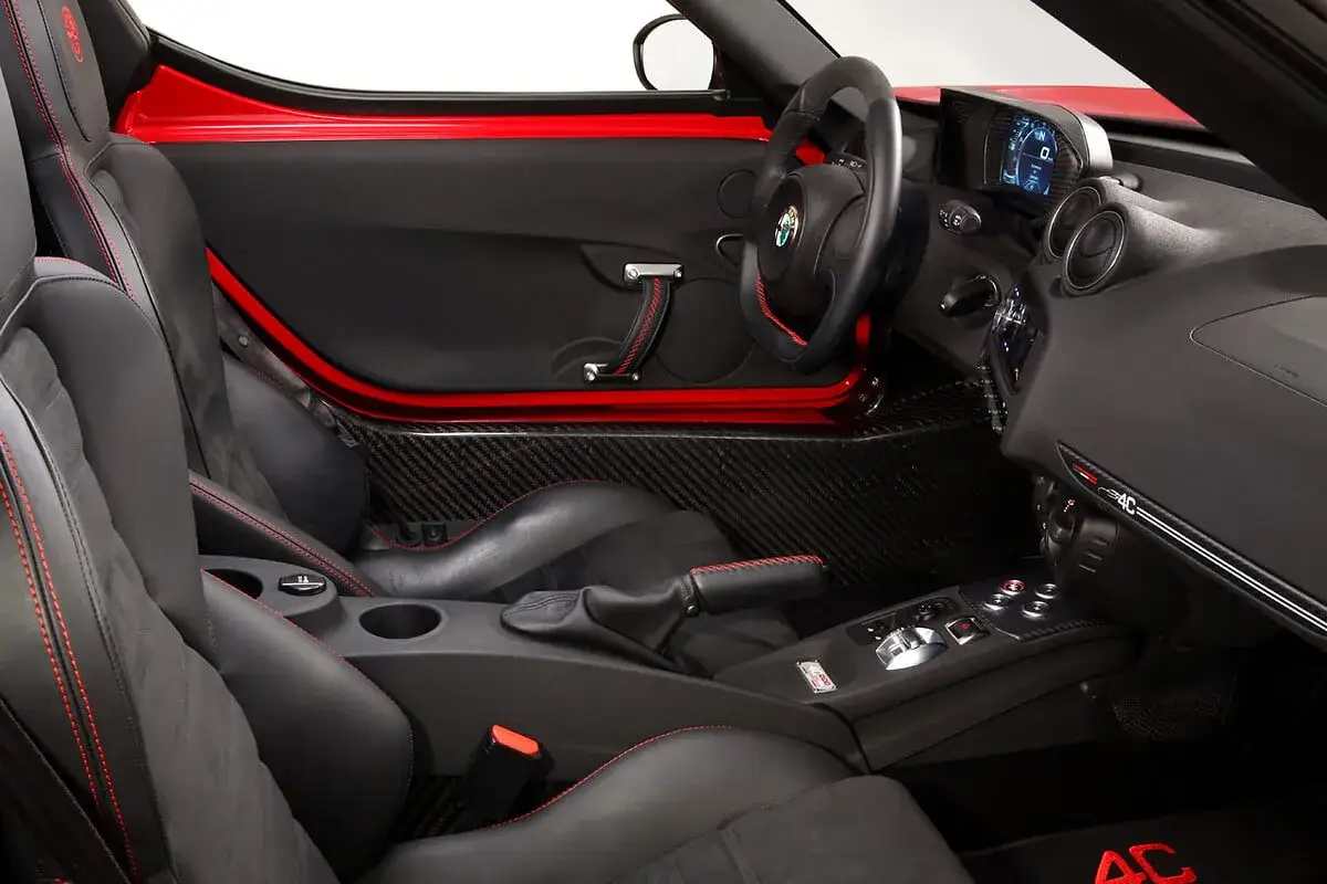 Wnętrze sportowego Alfa Romeo 4C z czarnymi fotelami, czerwonymi przeszyciami i elementami z włókna węglowego.